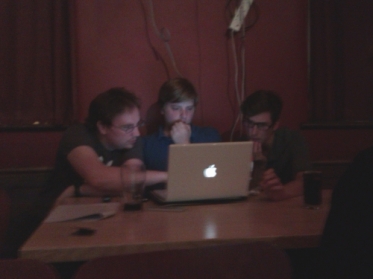 The men sit behind an Apple laptop discussing something