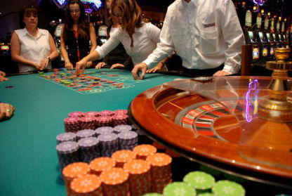 Four people stand around a roulette table